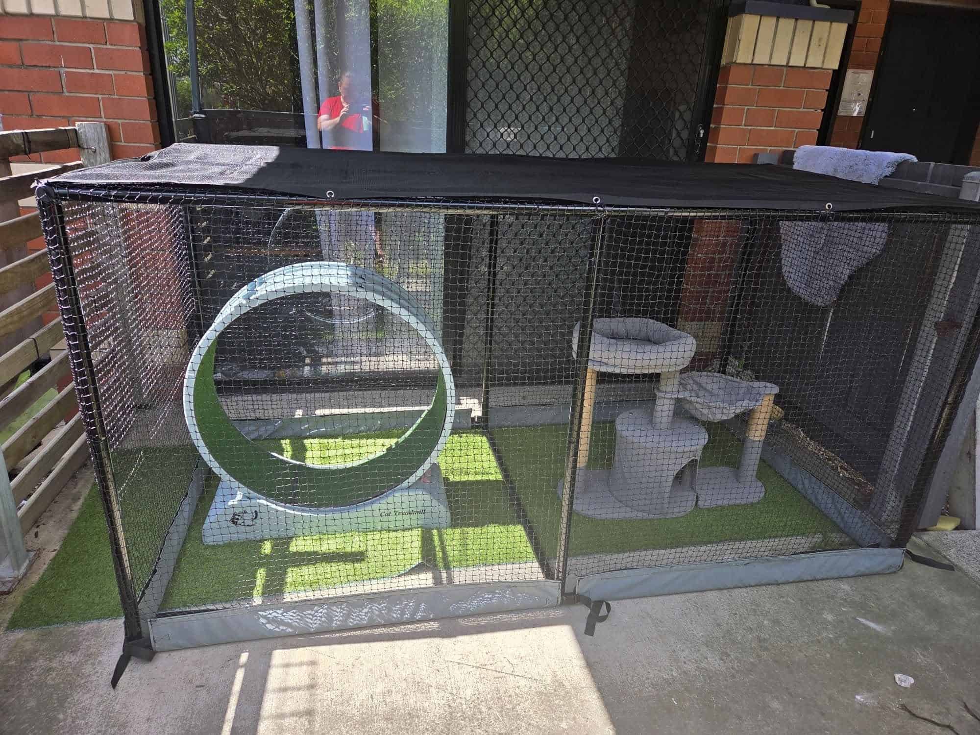 An outdoor cat net enclosure with cat climbing objects setup inside.