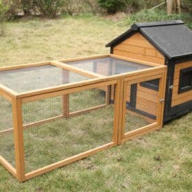 A brown and black timber guinea pig hutch sitting outdoors on grass.