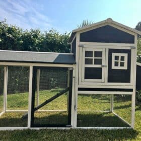 A large charcoal timber rabbit hutch sitting on grass with a clear blue sky background.